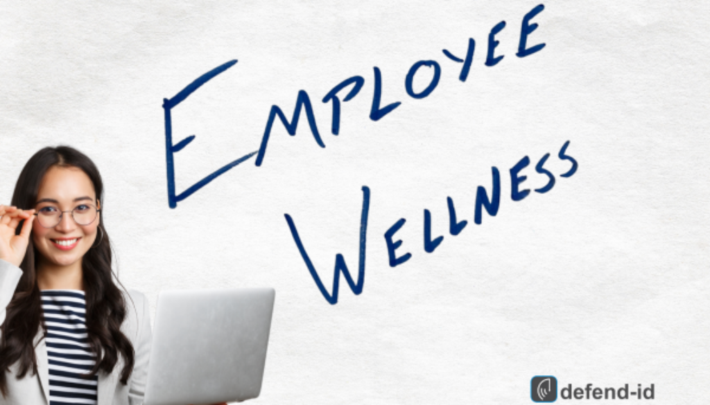 A smiling woman with glasses holds a laptop, standing next to the handwritten phrase "Employee Wellness" on a white background, with the defend-id logo in the corner.