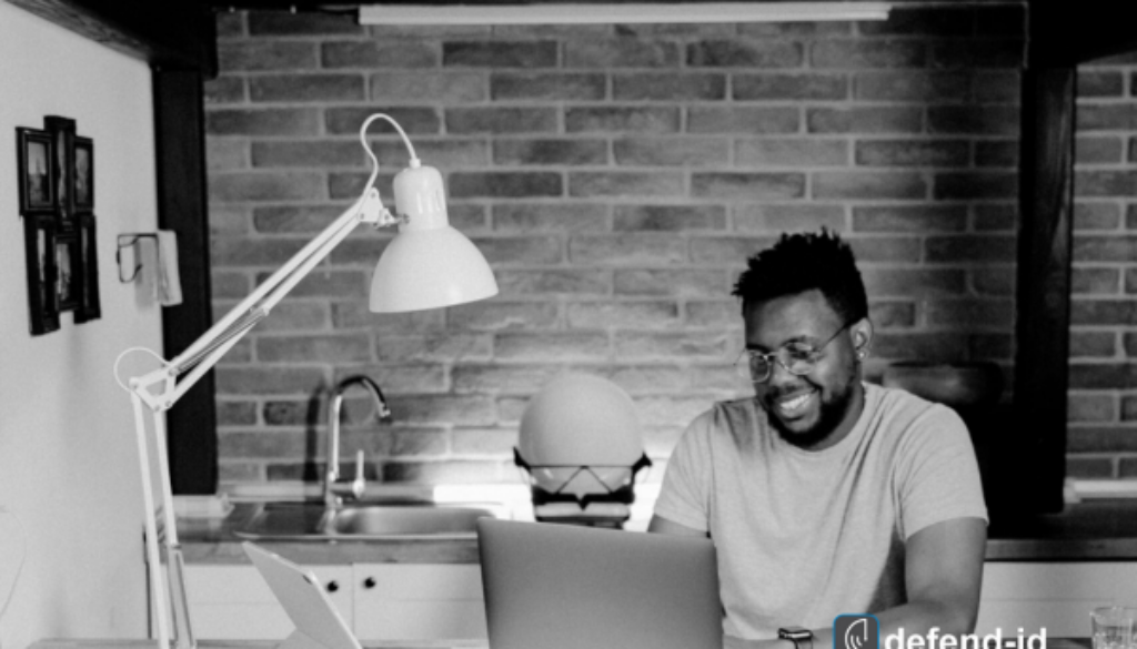 Man banking online from home on a laptop—defend-id logo reminds users to secure sessions with a VPN for online banking.