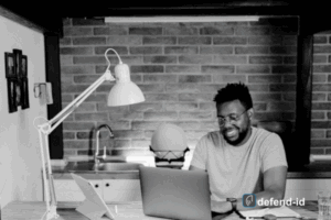 Man banking online from home on a laptop—defend-id logo reminds users to secure sessions with a VPN for online banking.